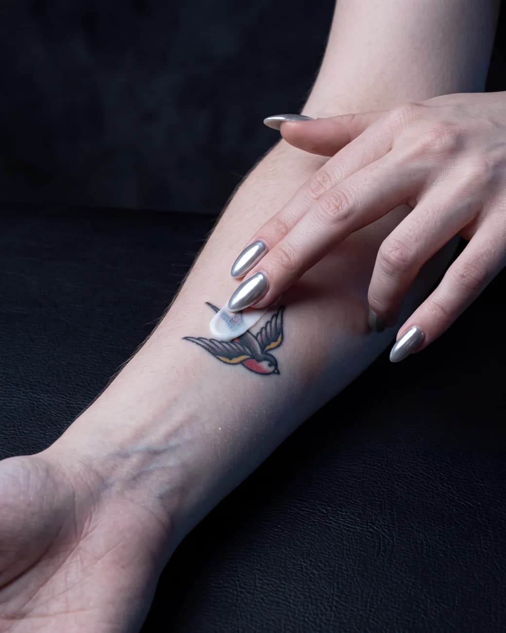 A fingertip of VITIUM Tattoo Butter being smoothed onto a healed swallow tattoo on a forearm