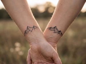 Couple holding hands showing matching mountain tattoos on wrists