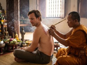 Traveller getting traditional Sak Yant tattoo from Thai Buddhist master demonstrating tattoo tourism