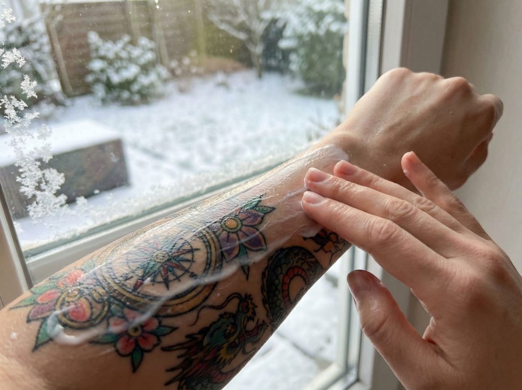 Close-up of tattooed arm being moisturised during cold winter months to prevent dry skin and ink fading